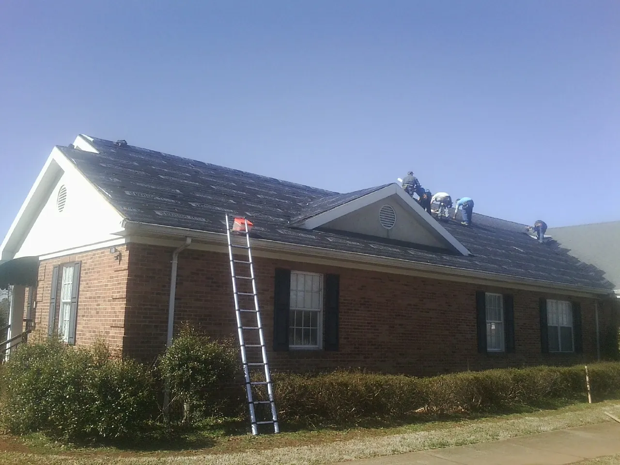 Crew tearing shingles off a brick ranch roof with a ladder set — Metal Roof Repair work by our crew in Inman