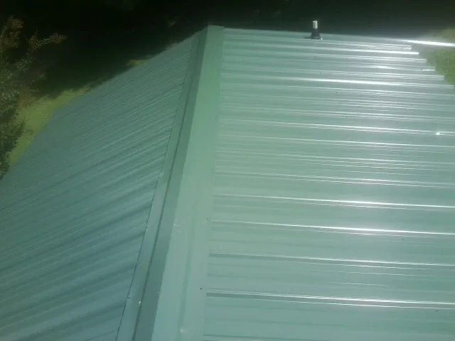 New green metal panels meeting at the ridge of a roof — Flat Roof Repair work by our crew in Inman