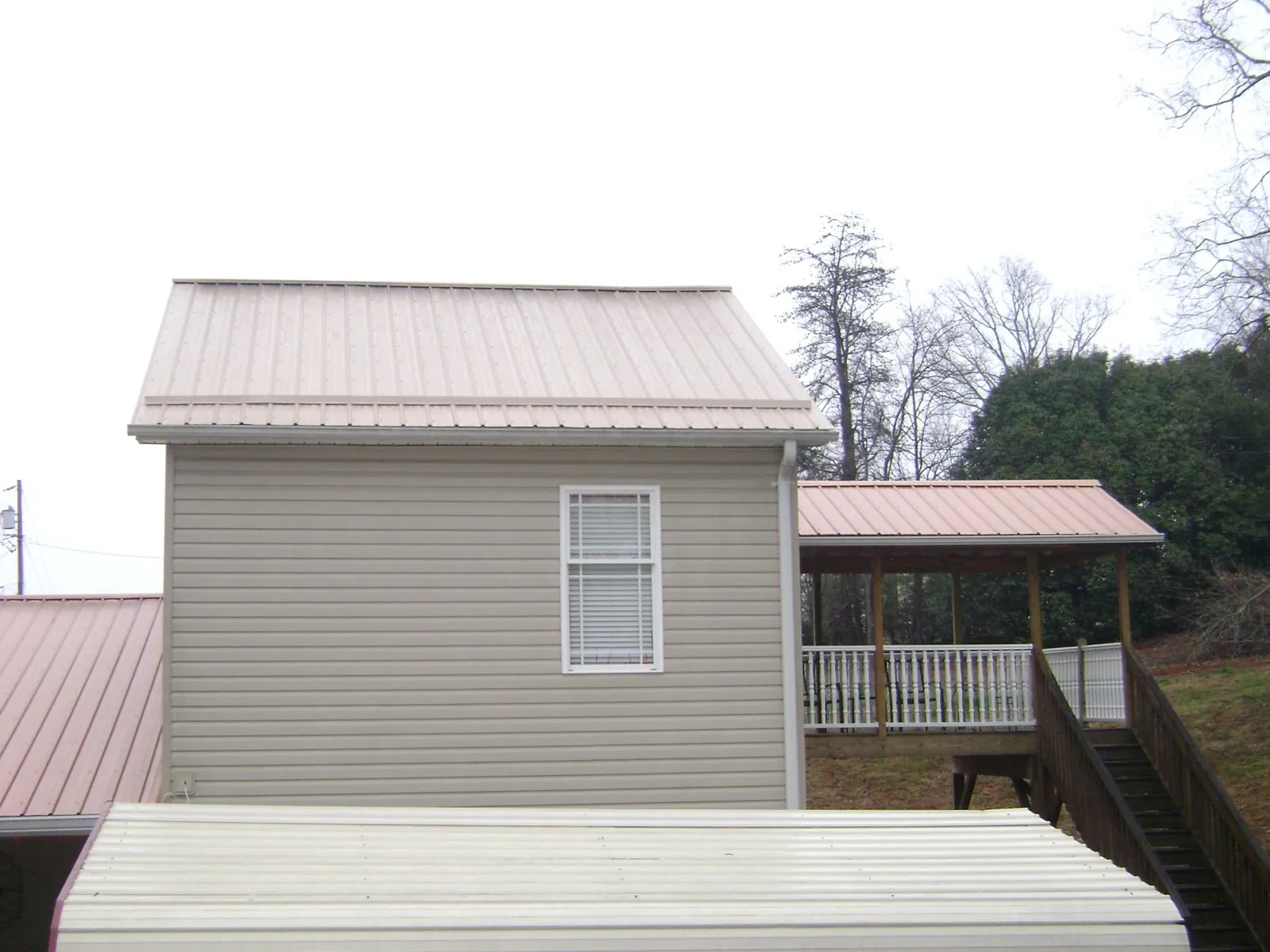 Tan metal roofs on a two story addition and attached porch, from a Roof Replacement job in Inman